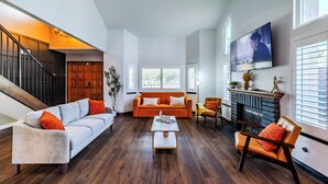 A spacious living room with a staircase, a fireplace, and a television mounted on the wall.