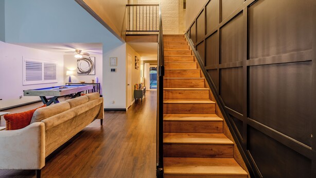 A modern interior with a wooden staircase, a sofa, and a pool table.