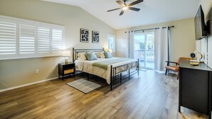 A bedroom with a bed, bedside tables, a ceiling fan, and a view of the outdoors.