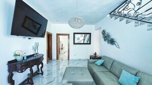 A living room with a large sectional sofa, a console table with decorative items, a flat-screen TV mounted on the wall, and a chandelier. - Luxury Villa Tavares Bautistas (Puerto Plata)