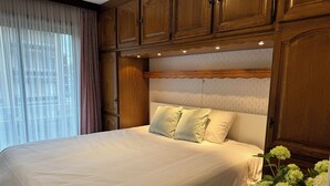 Un grand lit avec du linge de lit blanc, une tête de lit en bois et un vase de fleurs sur la table de chevet.