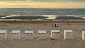 Une plage avec des structures blanches, peut-être des cabanes de plage, et quelques personnes au loin.