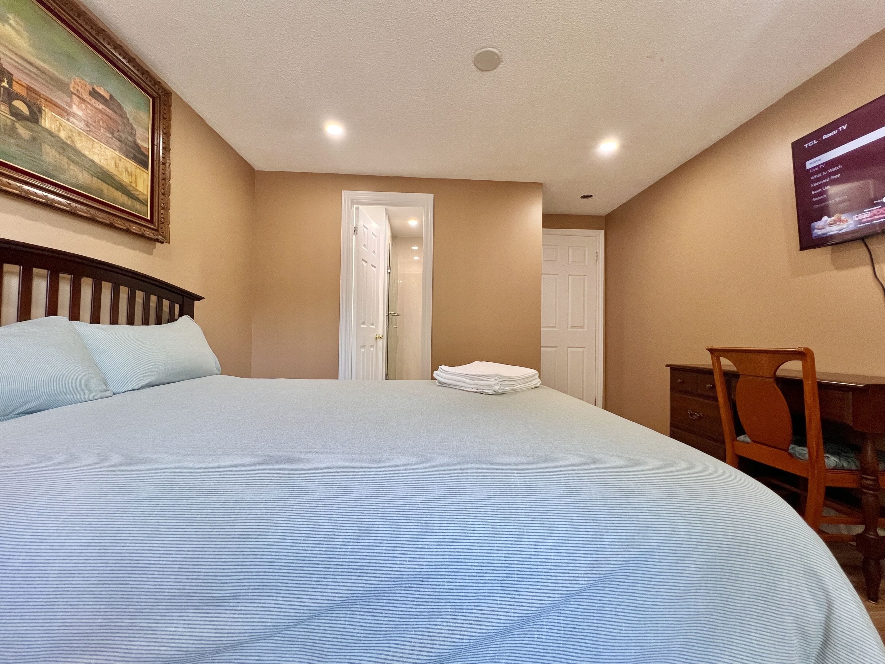 Habitación de hotel con cama, una silla, un escritorio, televisor y una puerta.