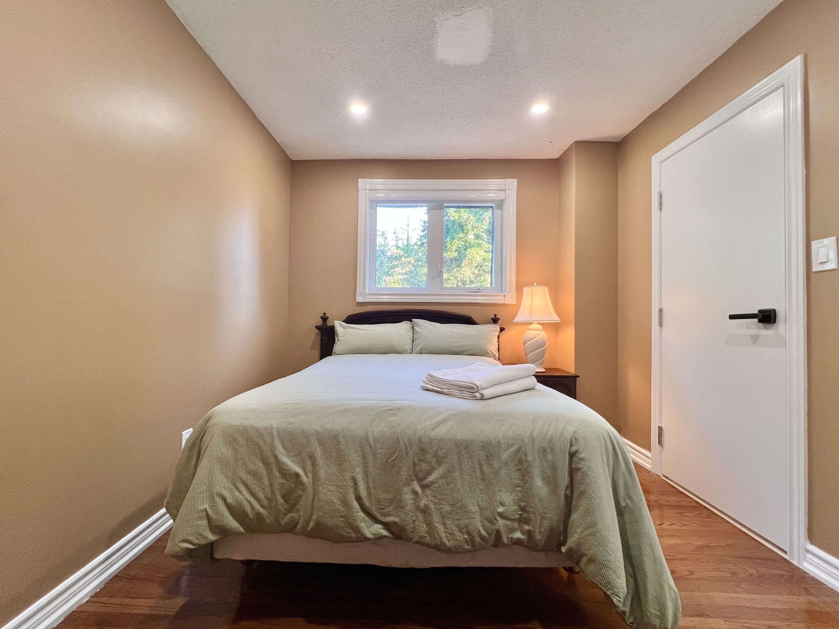 A bedroom with a bed, a window, a nightstand, and a door.