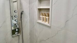 Um chuveiro com um chuveiro manual, painel de controle fixado na parede e um prateleira com artigos de higiene.