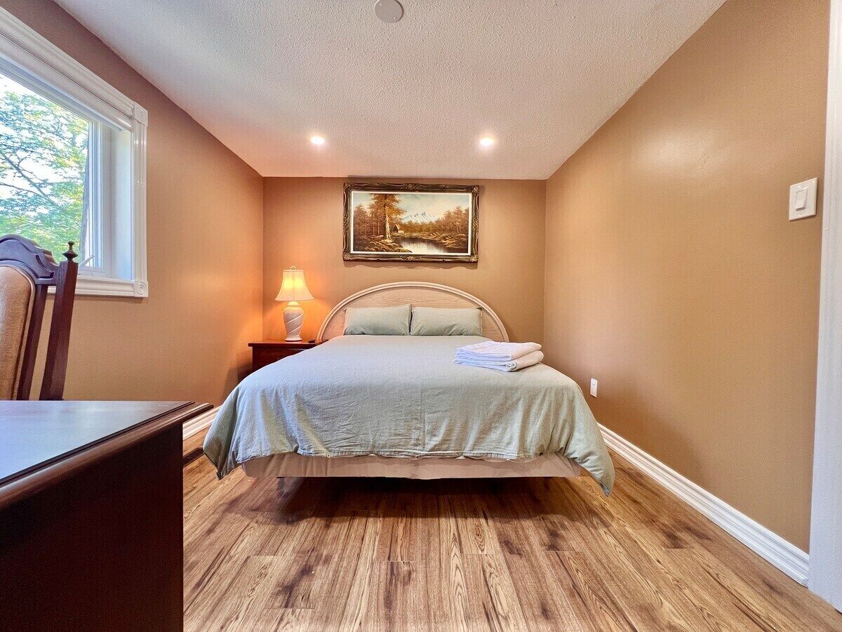 Un dormitorio con cama, mesita de noche, lámpara y un cuadro en la pared.