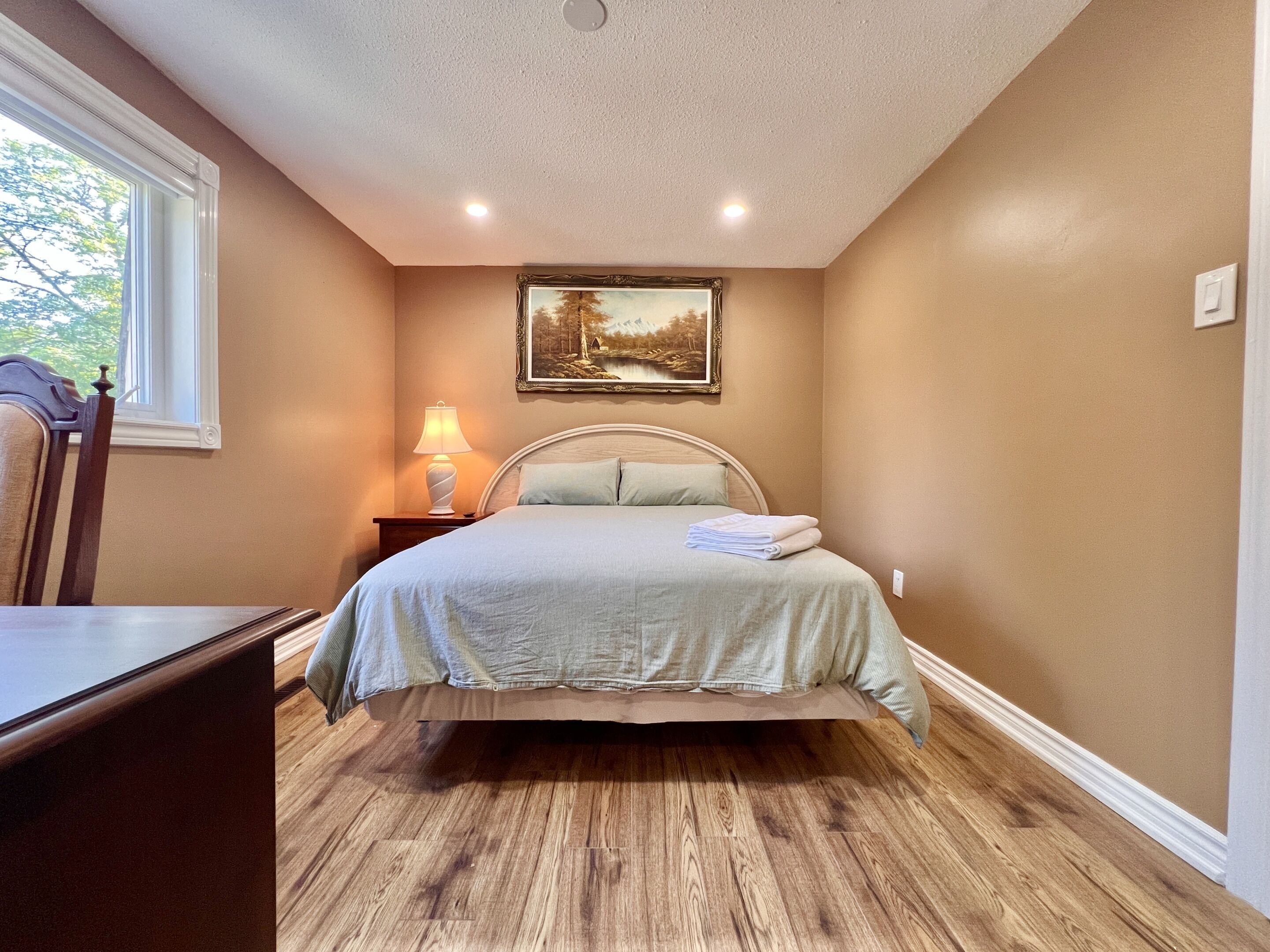 Un dormitorio con cama, mesita de noche, lámpara y un cuadro en la pared.