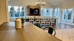 A spacious dining area with a large wooden table, a TV mounted on a stone wall, and a chandelier. - The Bavaria Farmhouse - 30 Acre Estate (Chaska)