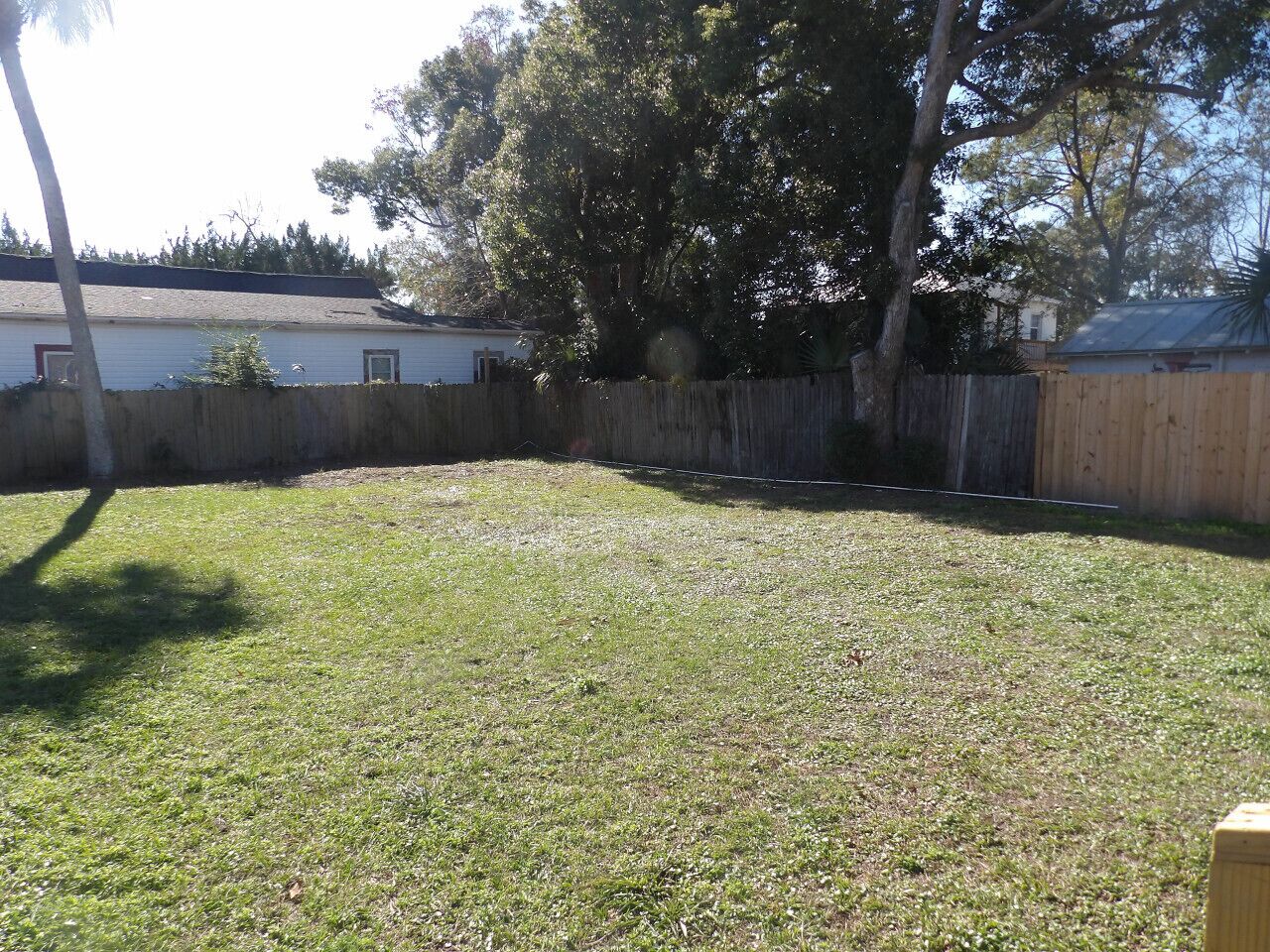 A backyard with a wooden fence, a grassy lawn, and a house in the background.