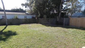 A backyard with a wooden fence, a grassy lawn, and a house in the background.