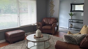 A living room with a brown leather sofa, a glass coffee table, and a grey rug.