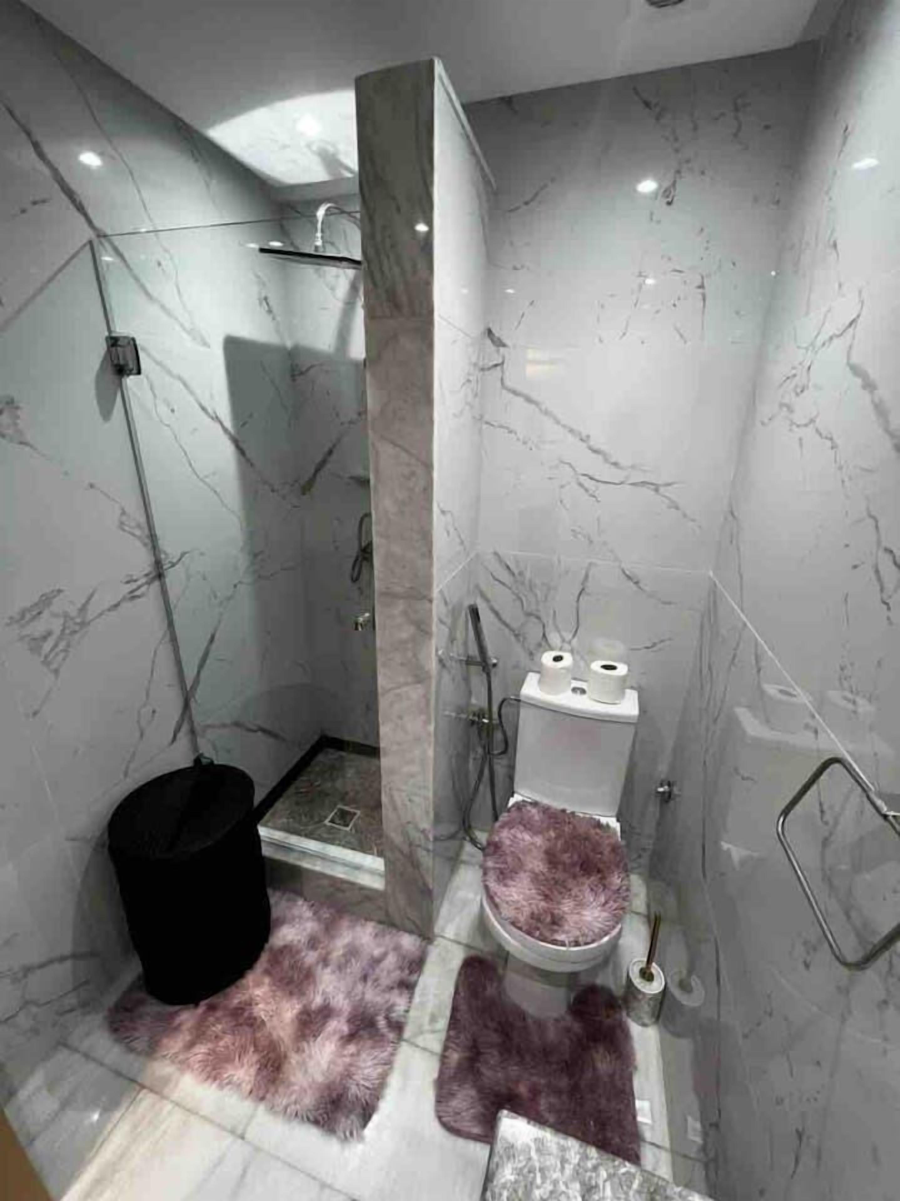 A modern bathroom with a shower, toilet, and marble walls.