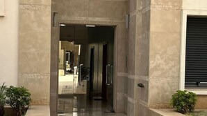 Una entrada moderna de edificio con puerta de cristal, un picaporte metálico y una pequeña planta en maceta al lado.