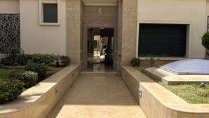 Una entrada de edificio con un vestíbulo cubierto, un portón de garaje y un pequeño jardín.
