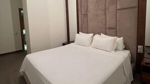 Una cama grande y bien hecha en una habitación de hotel moderna, con un cabecero amplio y acolchado y una paleta de colores neutros.