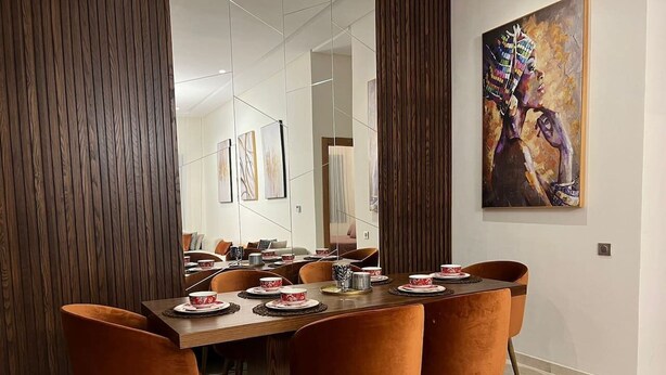 Un comedor con una larga mesa de madera dispuesta para seis personas, rodeado de sillas naranjas.