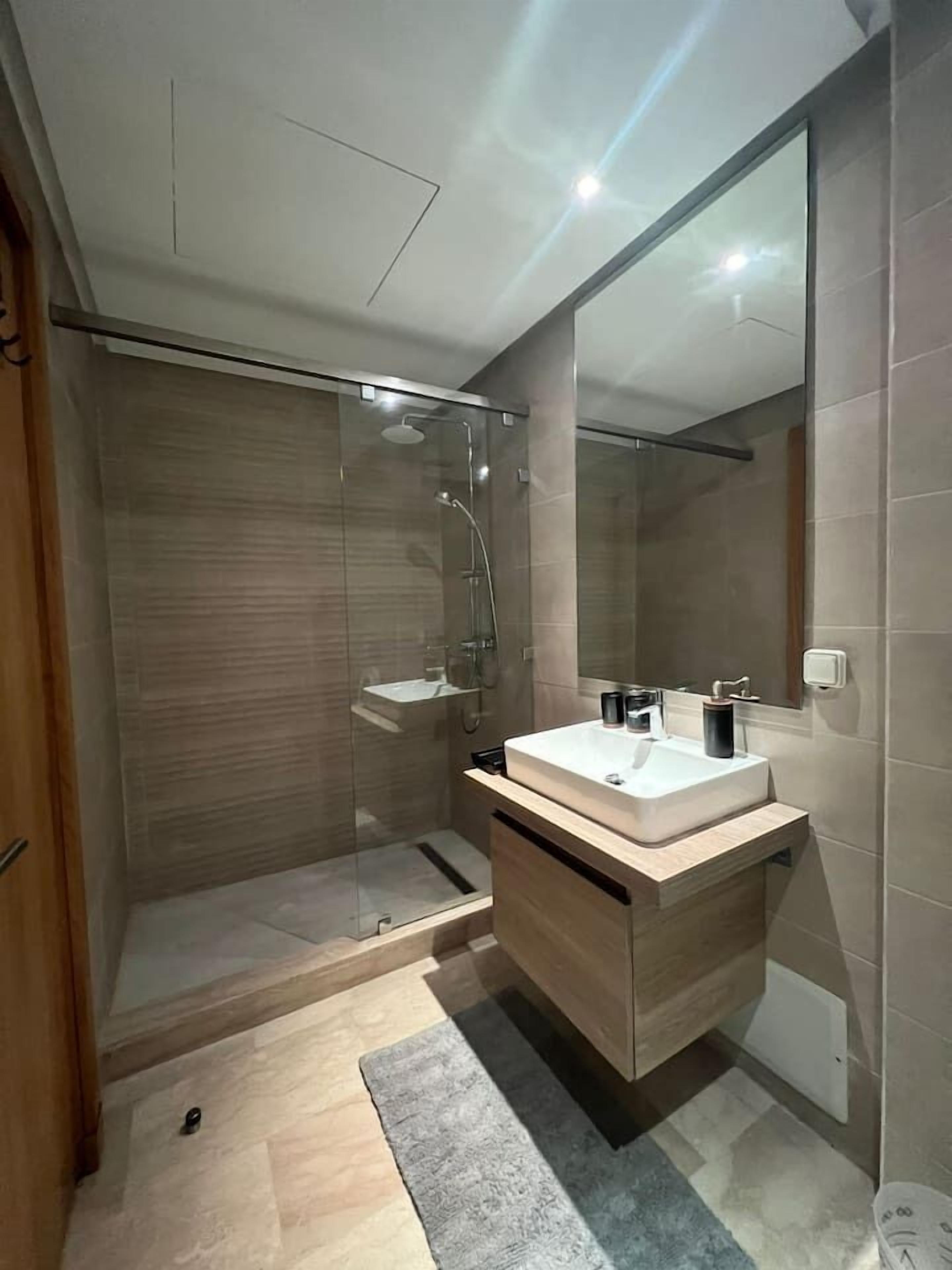 A modern bathroom with a glass-enclosed shower, a wooden vanity with a sink, and a large mirror.