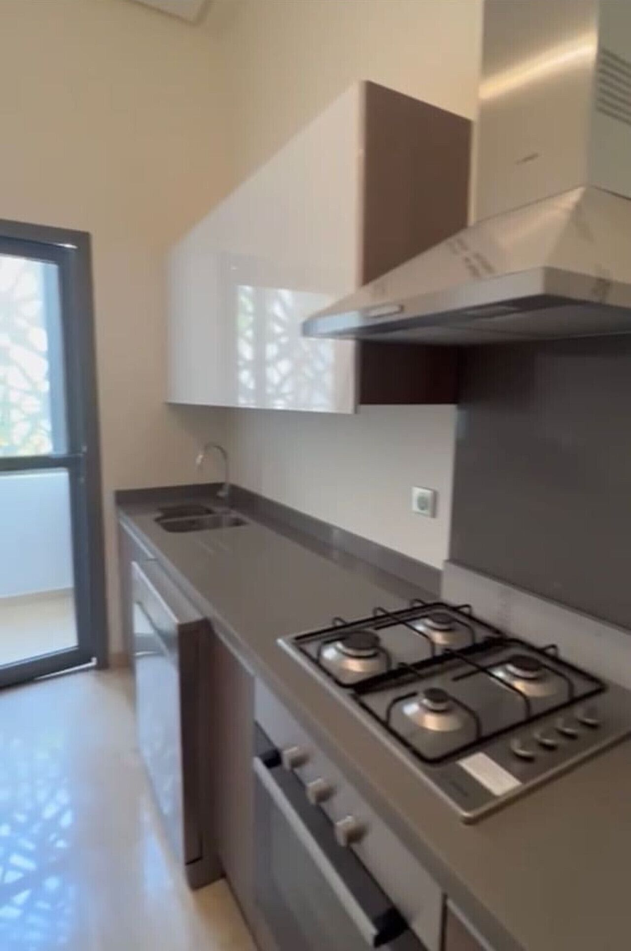 Une cuisine moderne équipée d’une cuisinière à gaz, de meubles en acier inoxydable et d’une porte-fenêtre coulissante donnant sur un balcon.