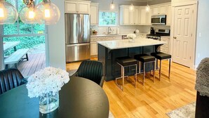 A modern kitchen with white cabinets, stainless steel appliances, and a central island with bar stools. - Modern House in Clifton Gaslight - 3 BR 3BA with Walkable Shops and Restaurants (Cincinnati)