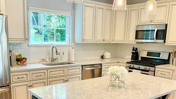 A modern kitchen with white cabinetry, a granite countertop, stainless steel appliances, and pendant lighting. - Modern House in Clifton Gaslight - 3 BR 3BA with Walkable Shops and Restaurants (Cincinnati)