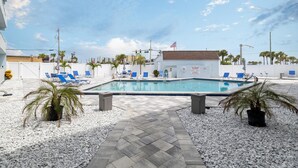 Un área de piscina con terraza de baldosas, palmeras y sillas de descanso azules.