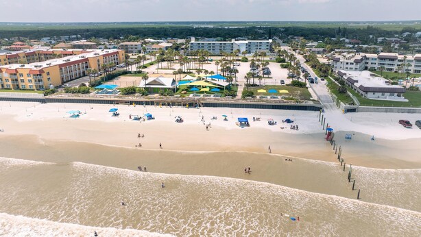 Un resort frente a la playa con varias construcciones, arena y sombrillas.