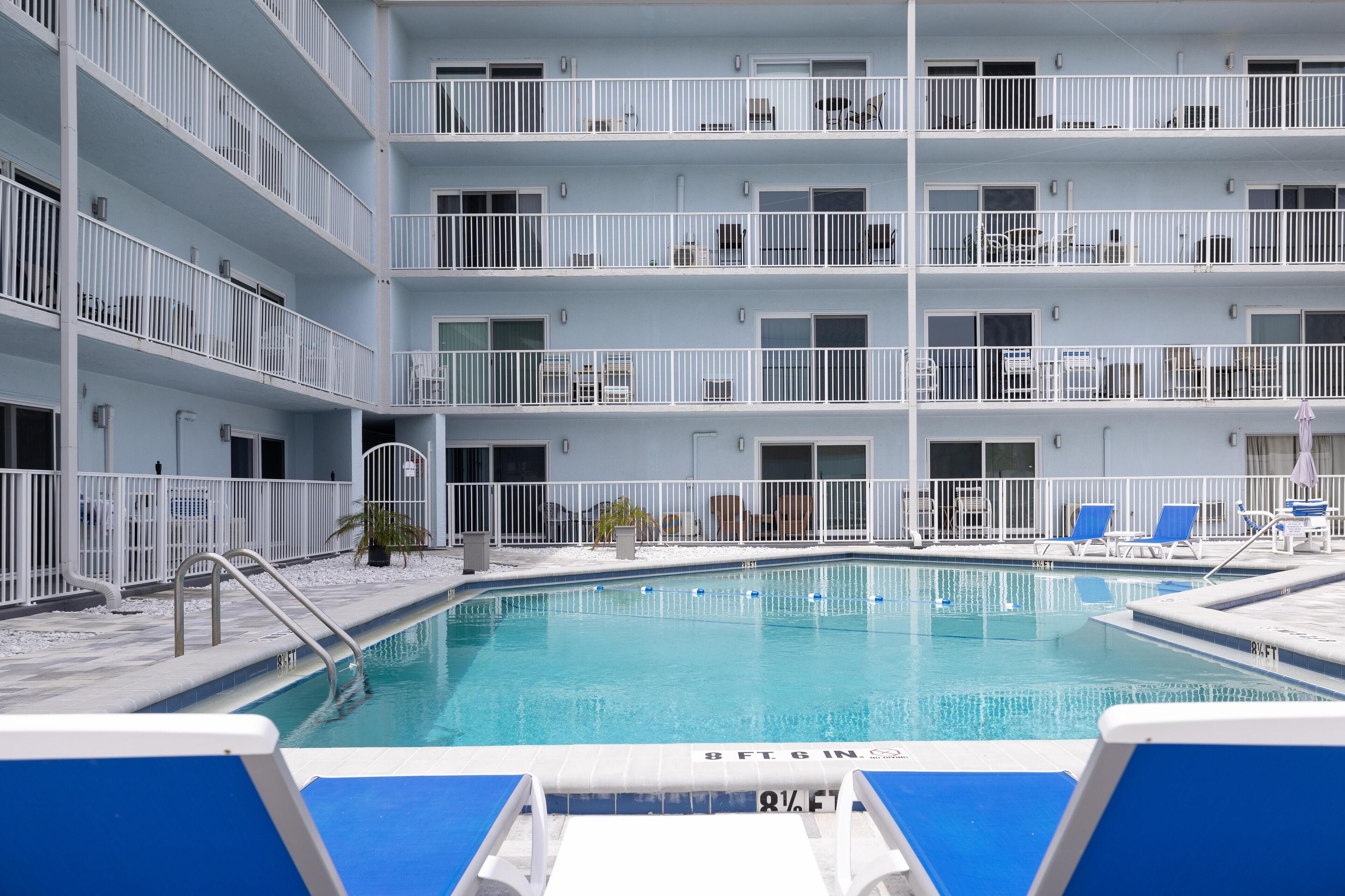 A multi-level hotel with a swimming pool, balconies, and lounge chairs.