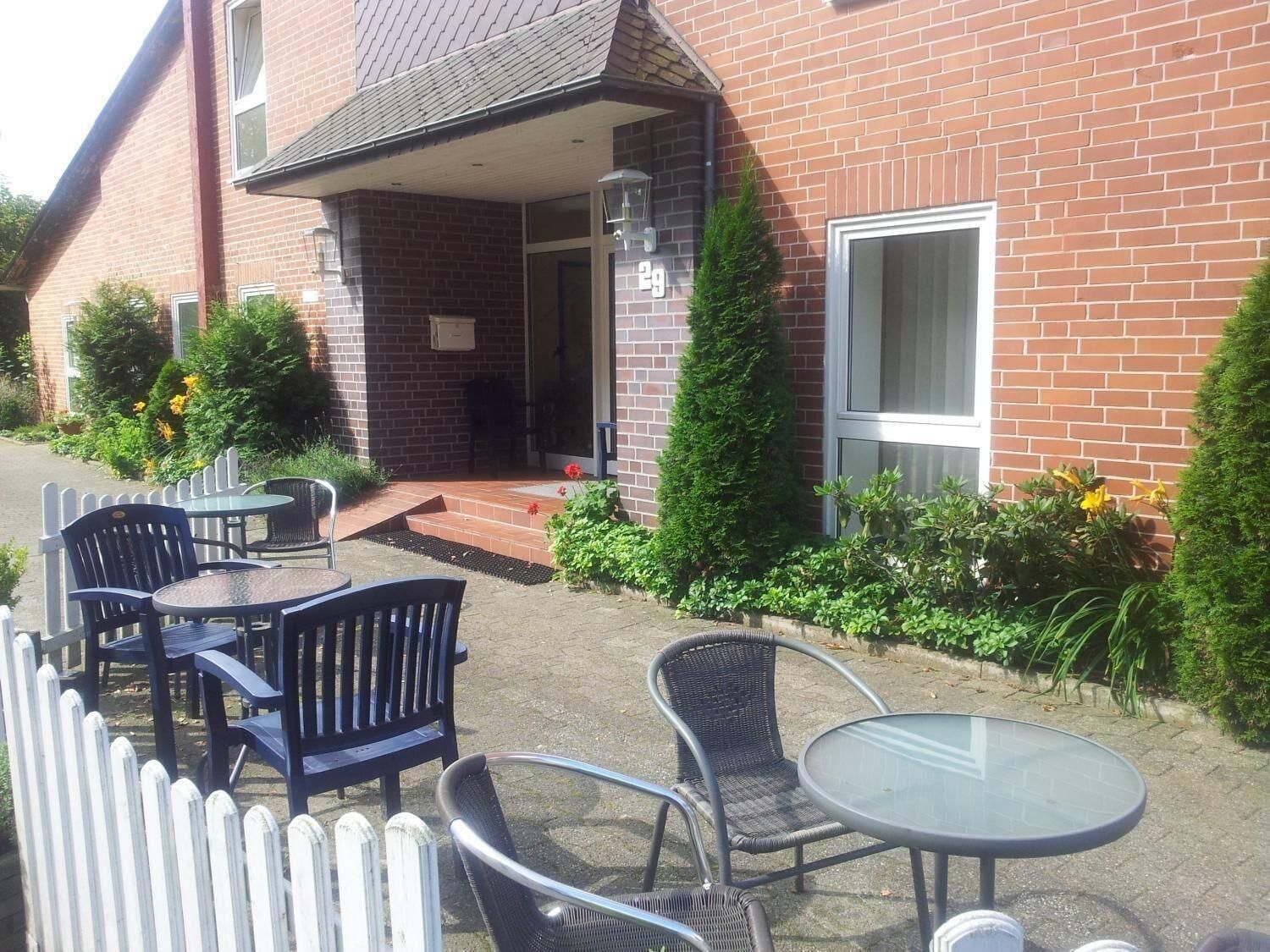 An outdoor seating area with tables and chairs, a brick building, and a white picket fence.