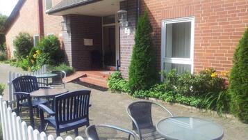 An outdoor seating area with tables and chairs, a brick building, and a white picket fence.