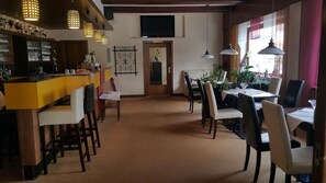 Un restaurant amb zona de bar, taules, cadires i llums penjants.