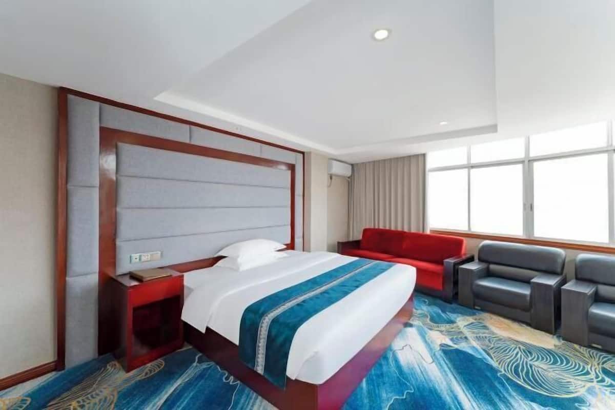 Une chambre d’hôtel avec un grand lit, un canapé rouge et plusieurs fauteuils.
