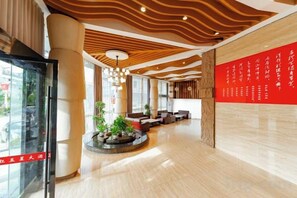 Un hall de hotel con una zona de estar central, un mostrador de recepción y una gran pared roja con texto.
