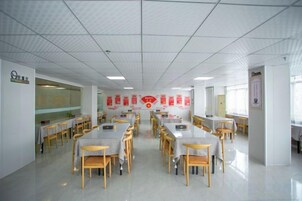 A spacious dining area with multiple tables and chairs, a tiled ceiling, and red signage on the walls.
