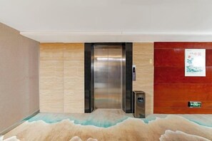 Un ascensor con acabado metálico, un cubo de basura fijado a la pared y un cartel en la pared.
