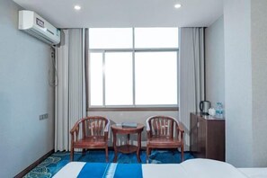 A hotel room with a bed, two wooden chairs, a small table, a window with curtains, and a minibar. - Hongwuxing International Hotel (Ruijin)
