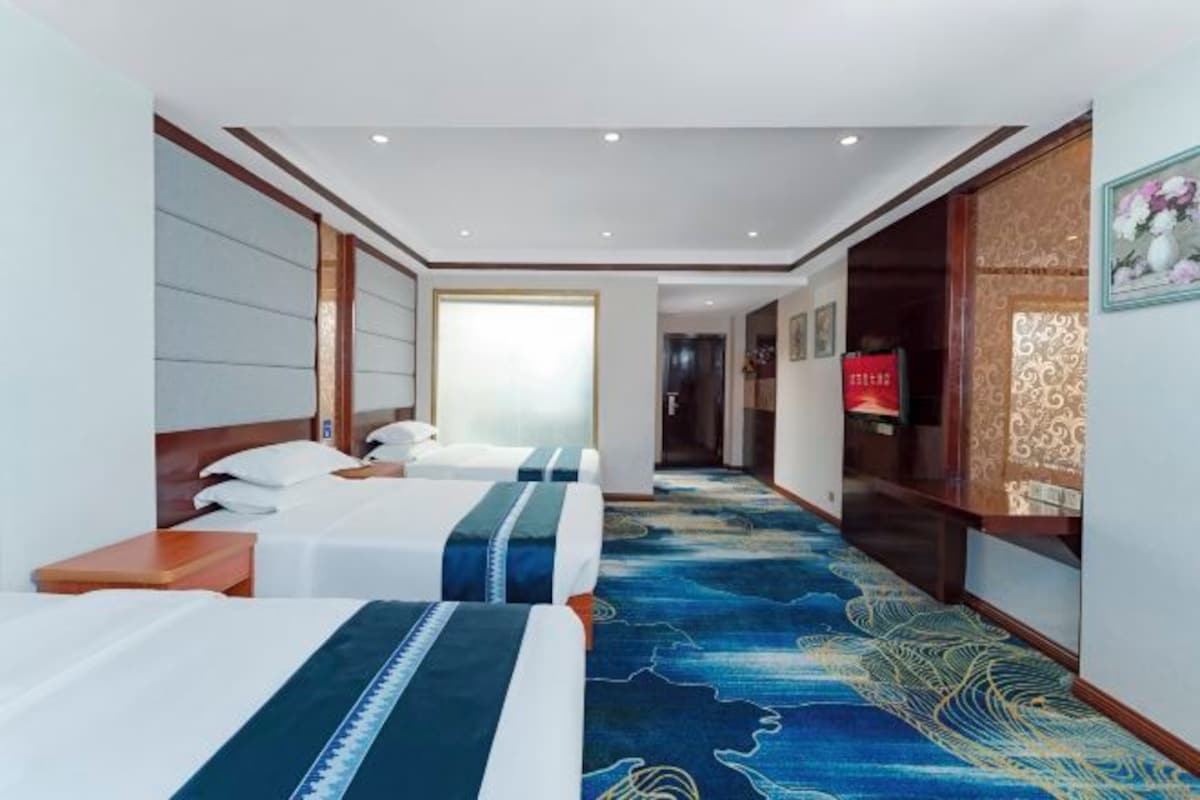 A hotel room with two beds, a large window, a carpeted hallway, and a reception desk.