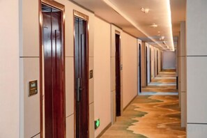 Un couloir d’hôtel avec des portes des deux côtés, une moquette à motifs et un panneau de signalisation verte indiquant la sortie.