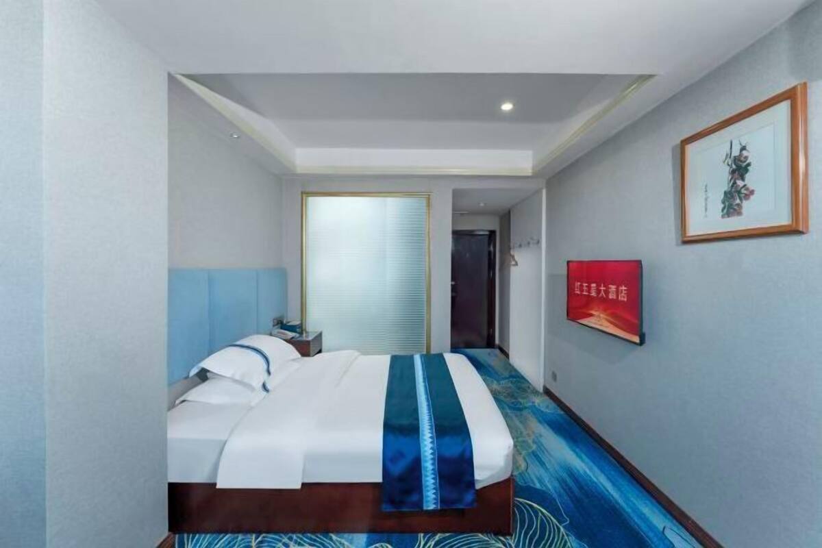 Une chambre d’hôtel avec un lit, une table de chevet, un tableau encadré et un panneau rouge sur le mur.