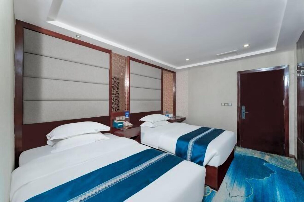 A hotel room with two beds, a wooden headboard, a nightstand, and a door.