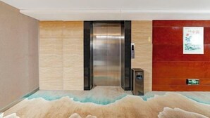 Een lift in een gang met een vloerbedekking met een structuur en een bordje aan de muur.