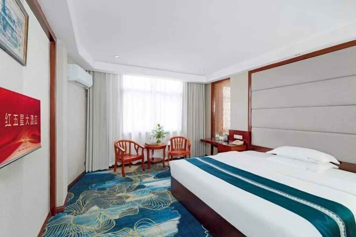 Une chambre d’hôtel avec un grand lit, un bureau, deux chaises et une fenêtre avec des rideaux.