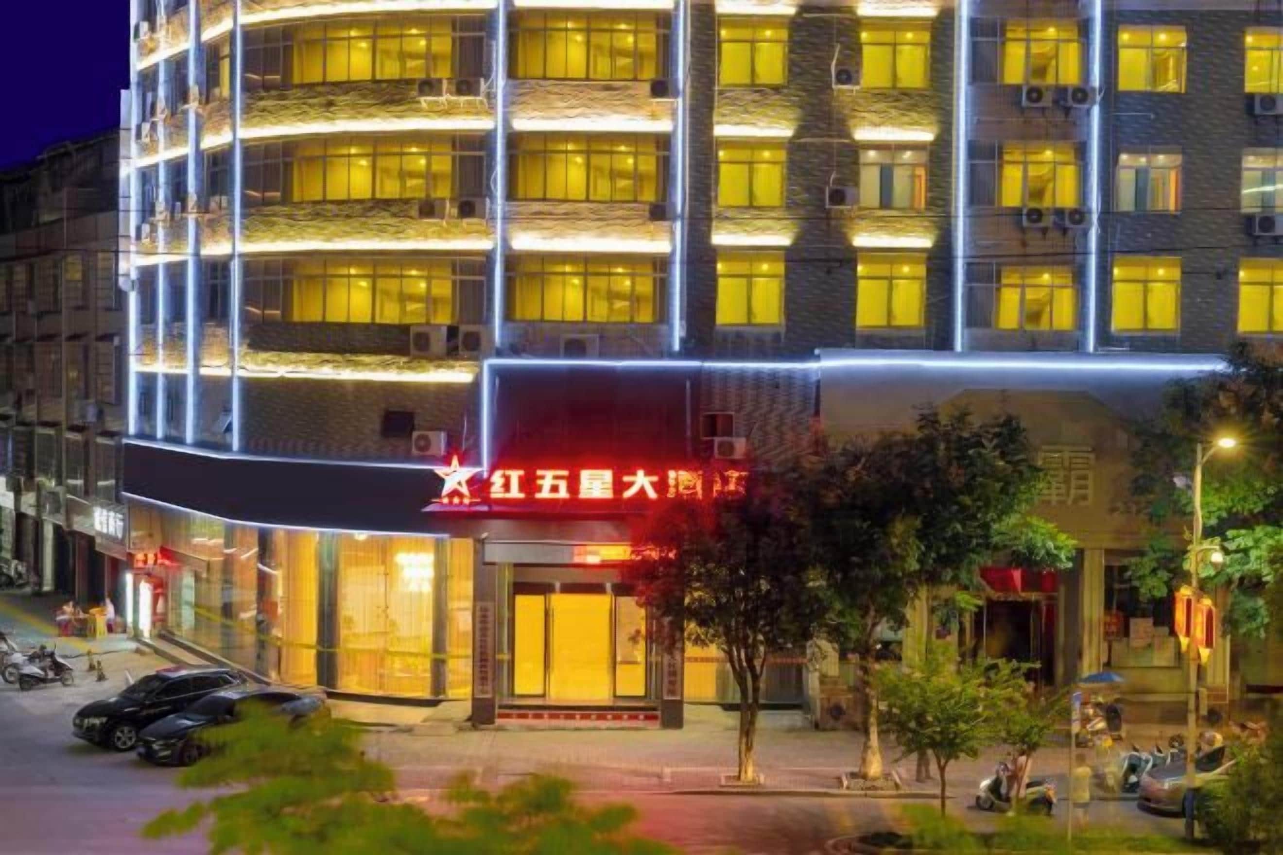 A multi-story hotel with a prominent red sign, balconies, and a well-lit facade.