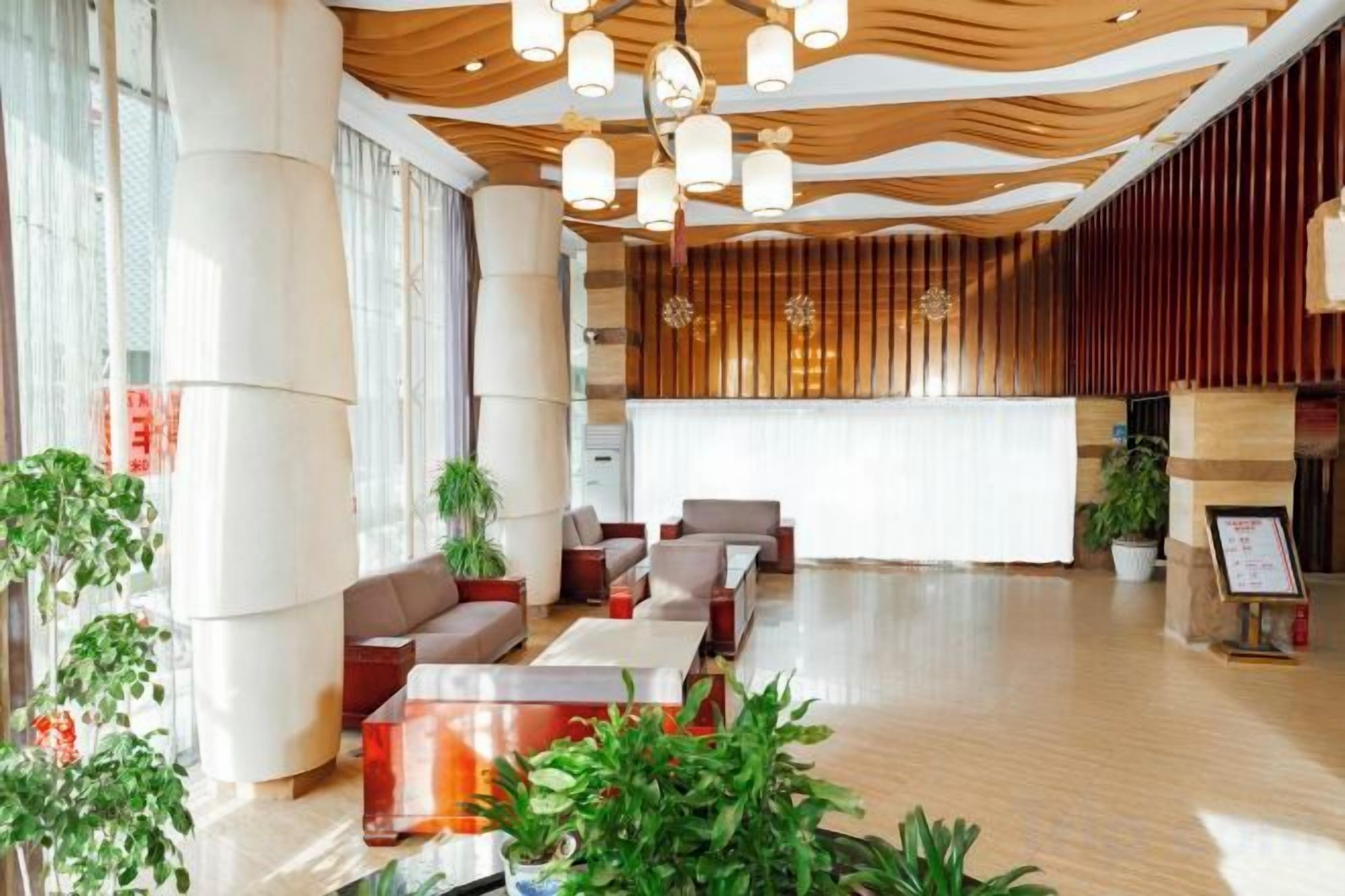 A modern hotel lobby with a reception desk, seating area, and large windows.