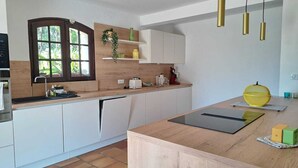 A modern kitchen with white cabinets, a wooden countertop, a built-in dishwasher, and a window with a view of greenery.
