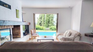 A room with a bed, a television, a table, a chair, and a view of a swimming pool.