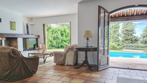 A living room with a fireplace, a sofa, a table, and a view of a swimming pool.