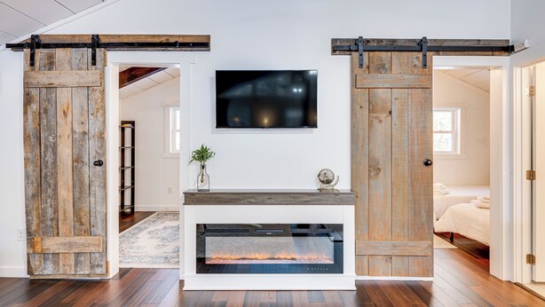 A modern living room with a fireplace, wooden sliding doors, and a TV mounted on the wall. - 9 Mi to Cranmore Mtn Resort: 'Lofty Dreams' Cabin (Center Conway)