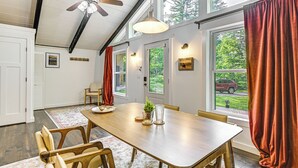 A dining area with a wooden table, chairs, a ceiling fan, and large windows with curtains. - 9 Mi to Cranmore Mtn Resort: 'Lofty Dreams' Cabin (Center Conway)