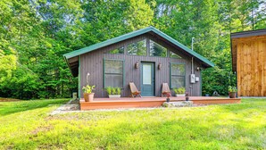 A wooden cabin with a green roof, large windows, and a porch with chairs and potted plants. - 9 Mi to Cranmore Mtn Resort: 'Lofty Dreams' Cabin (Center Conway)