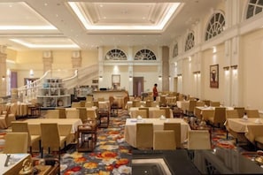A hotel dining area with multiple tables and chairs, a staircase, and a view of the lobby. - Xiqiao Mountain Qiaoyue Resort Hotel (Foshan)